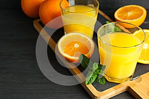 Cutting board with orange juice, mint and oranges on wooden table against black background, space for text