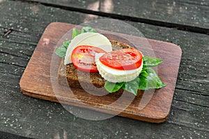 Cutting board with organic homemade cheese sandwich, bran bread, tomato and basil on an old dark wooden background