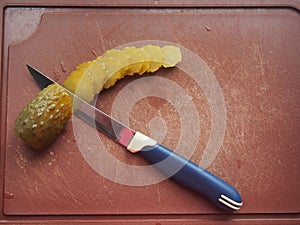 On the cutting Board are a pickle and a knife. The pickle is cut into slices