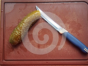 On the cutting Board are a pickle and a knife. The pickle is cut into slices