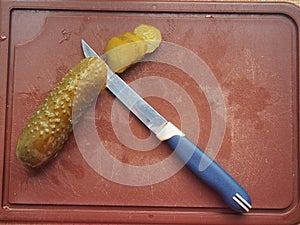 On the cutting Board are a pickle and a knife. The pickle is cut into slices