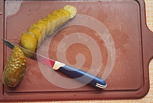 On the cutting Board are a pickle and a knife. The pickle is cut into slices