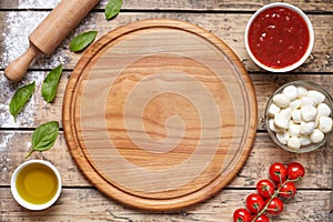 Cutting board with pizza ingridients: mozzarella, tomatoes sauce, basil, olive oil, cheese, spices. Italian pizza