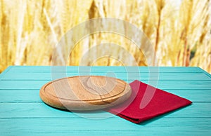 Cutting board for pizza and red napkin tablecloth on blue wooden kitchen table. Blur rye yellow bokeh background. Copy space.