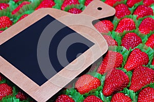 A cutting board with a place for text is placed on a strawberry background. Lots of red ripe delicious strawberries are laid out