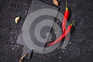 Cutting board and Red hot chili pepeprs on black stone background, top view