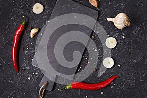 Cutting board and Red hot chili pepeprs on black stone background, top view