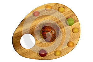 Cutting board in shape of an artist palette with multi-colored tomatoes on it; top view.