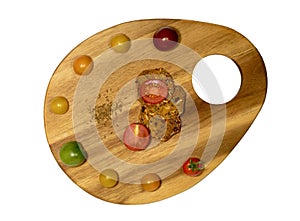 Cutting board in shape of an artist palette with multi-colored tomatoes on it; top view.