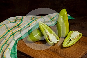 Cutting board with two whole and halves of green bell pepper and green kitchen towel on wooden background