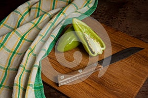 Cutting board with whole and halves of green bell pepper and green kitchen towel on wooden background