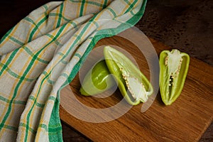 Cutting board with whole and halves of green bell pepper and green kitchen towel on wooden background