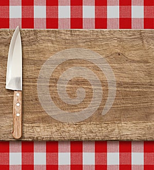 Cutting breadboard and kitchen knife. Cooking set over red gingham tablecloth.