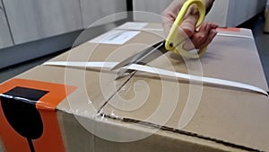 Cutting brown tape with scissors and sealing a cardboard box