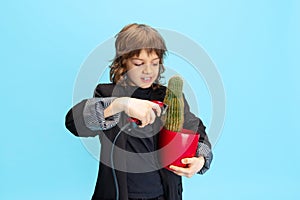 Cutting cactus. Comic portrait of little boy, kid in huge black jacket like barber having fun isolated over blue