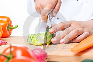 Cutting cucumber slices on a wooden board with a sharp knife