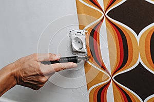 cutting the edges of a wallpaper surrounding a socket