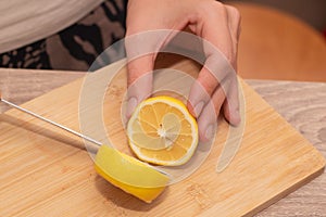 Cutting a Fresh Lemon on a Wooden Board. Hand slicing a yellow lemon on a bamboo cutting board