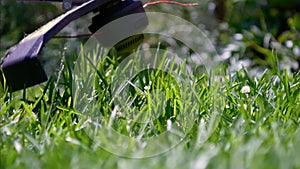 Cutting green grass with whipper snipper. Hand held grass trimmer mowing lawn. Grass shreds flying around in slow-mo