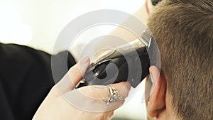 Cutting hair with electric razor in barbershop close up. Woman hairdresser working with client and doing male haircut