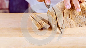 Cutting Homemade whole wheat and grain bread with knife bread, slices loaf on wooden board background.