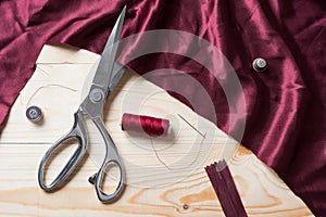 Cutting maroon fabric with a taylor scissors on wooden table