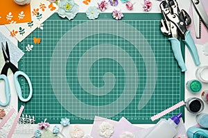 The cutting mat is surrounded by paper flowers, paper, tools and scrapbooking materials photo