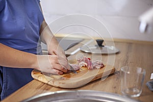 Cutting meat on a board, woman& x27;s hands with a knife. Unposed natural shot of a woman in the process of cooking in