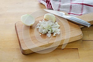 Cutting onions into small cubes with a kitchen knife on a wooden chopping board, selected focus, narrow depth of field