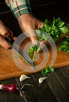 Cutting parsley with a knife on a cutting board. Cooking vegetable salad in the kitchen by the hands of a cook. The idea of a