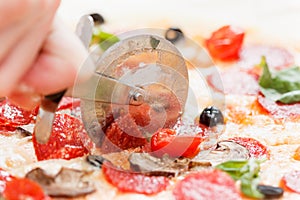 Cutting pepperoni pizza on slices with special knife.