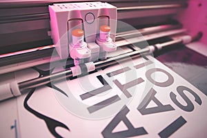 cutting plotter equiped with two adjustable blades makes adhesive lettering from black vinyl foil in energetic pink light