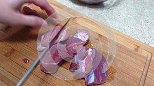 Cutting pork meat pieces with a knife on a wooden board