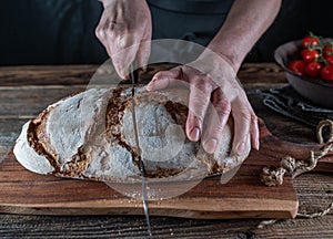 Cutting rustic loaf of sourdough bread by womans hand with a bread knife
