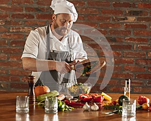Young Caucasian red-bearded man, chef cooking fresh vegetable salad in cafe, restaurant kitchen. Concept of a correct