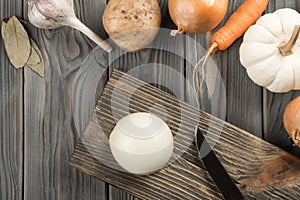 Cutting spicy onion with knife on kitchen wooden board. Whole white onion. Flat lay view. Vegetables layout on table.