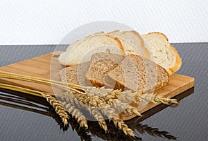 Cutting two types of bread with wheat ears on wooden Board