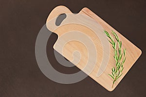 Cutting wooden board with a sprig of rosemary on a dark background