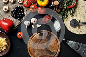 Cutting wooden board with traditional pizza preparation ingredients: cheese, tomatoes sauce, basil, olive oil, pepper