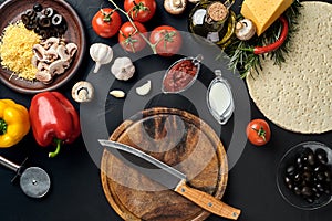 Cutting wooden board with traditional pizza preparation ingredients: cheese, tomatoes sauce, basil, olive oil, pepper