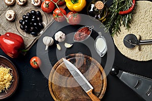 Cutting wooden board with traditional pizza preparation ingredients: cheese, tomatoes sauce, basil, olive oil, pepper