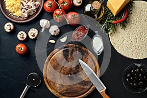 Cutting wooden board with traditional pizza preparation ingredients: cheese, tomatoes sauce, olives, olive oil, pepper