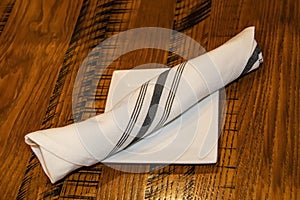 Cuttlery wrapped in a striped linnen napkin lying on a bread dish on a wooden table