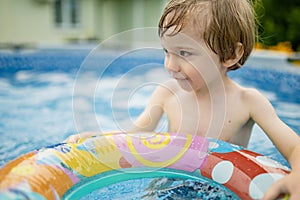 Cuty funny toddler boy having fun in outdoor pool. Child learning to swim. Kid having fun with water toys. Family fun in a pool