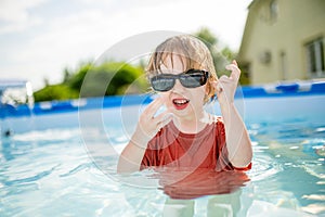 Cuty funny toddler boy having fun in outdoor pool. Child learning to swim. Kid having fun with water toys. Summer activities for