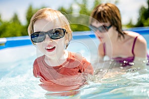 Cuty funny toddler boy and his teenage sister having fun in outdoor pool. Child learning to swim. Kid having fun with water toys.