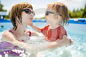 Cuty funny toddler boy and his teenage sister having fun in outdoor pool. Child learning to swim. Kid having fun with water toys.