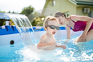 Cuty funny toddler boy and his teenage sister having fun in outdoor pool. Child learning to swim. Kid having fun with water toys.