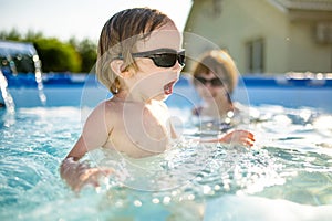 Cuty funny toddler boy and his teenage sister having fun in outdoor pool. Child learning to swim. Kid having fun with water toys.
