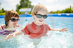 Cuty funny toddler boy and his teenage sister having fun in outdoor pool. Child learning to swim. Kid having fun with water toys.